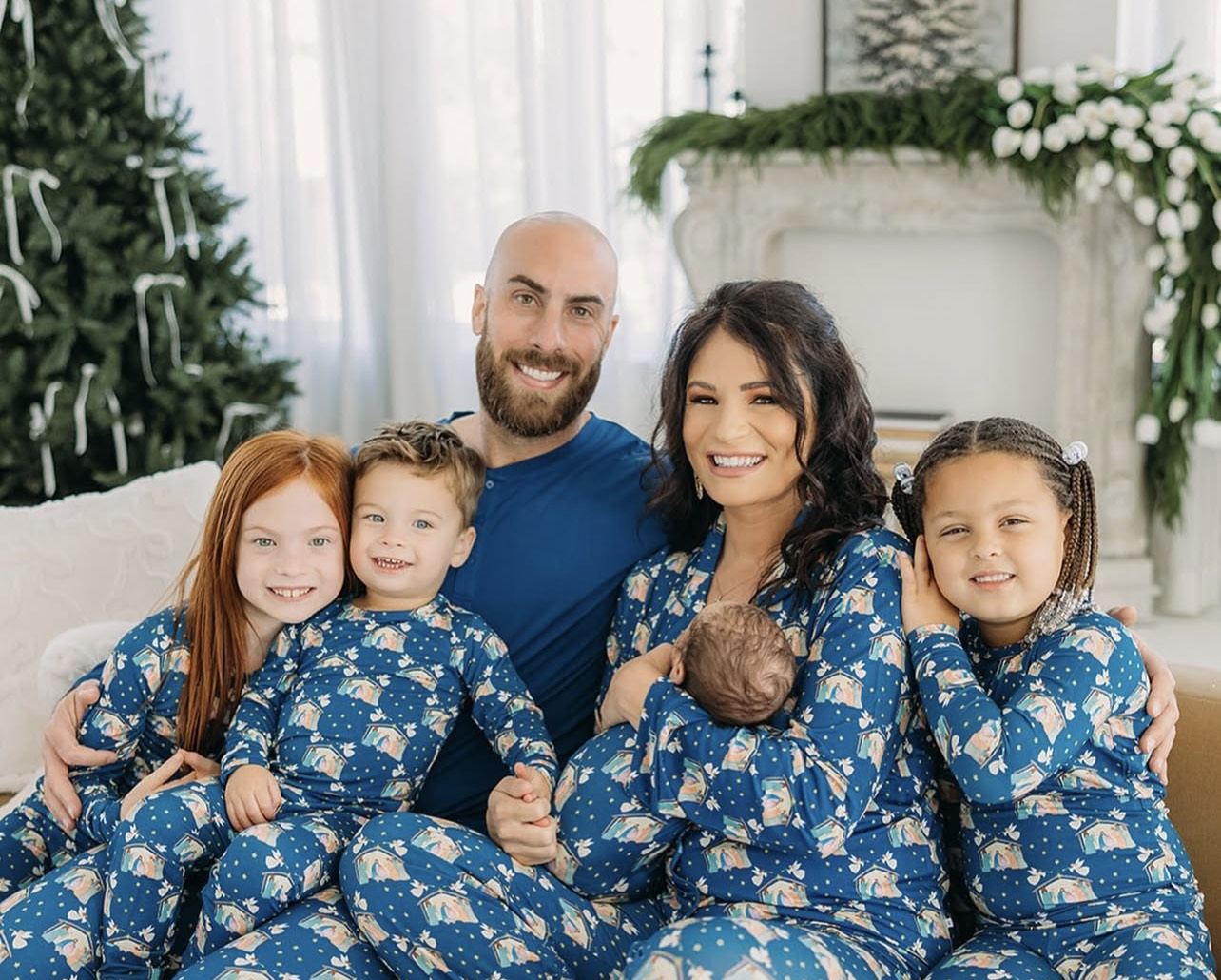 Family of five wearing matching blue pajamas in a festive living room with Christmas decorations.