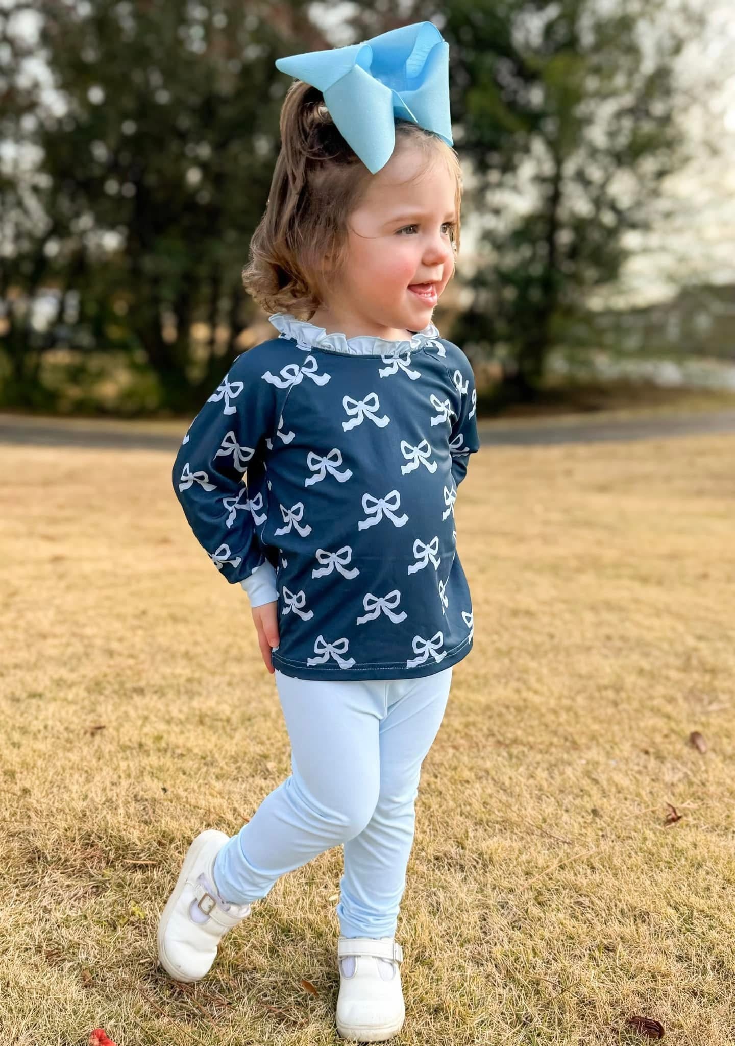 Child wearing a navy blue shirt with white bow pattern outdoors